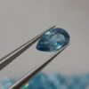 Pear-shaped faceted natural zircon gemstone held with tweezers by a gemologist, showing clarity and sparkle